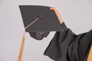 Beyaz arka planda mezuniyet şapkası takan yaşlı bir kadının eli.