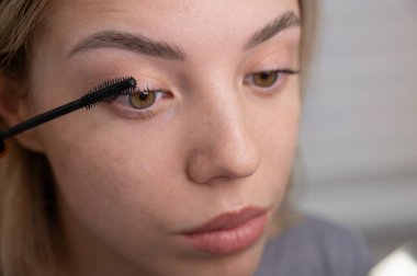 Genç bir kadının dikkatlice maskarasını kirpiklerine sürerken.