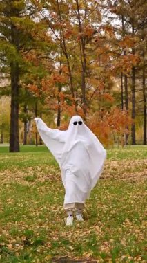 Hayalet kostümlü bir kadın sonbahar ormanında yürüyor. Cadılar Bayramı kostümü. Dikey video