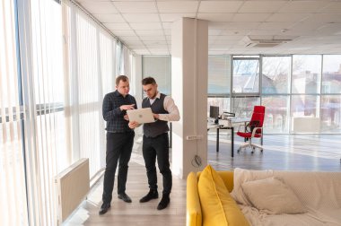 İki beyaz adam dizüstü bilgisayara bakıyor ve iş tartışıyorlar.