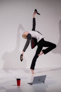 Beyaz arka planda iş elbisesiyle dans eden çıplak ayaklı balerin.