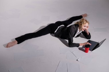 İş elbisesi giymiş bir balerin orta sicimle oturur, dizüstü bilgisayarda çalışır ve kahve içer. Bilgisayar başında esnek bir kadın çalışıyor..