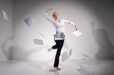 Takım elbiseli zarif bir balerin belgeleri fırlatır. İş kadını beyaz arka planda yalınayak dans ediyor..