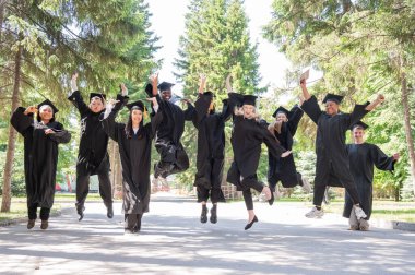 Mezuniyet elbiseleriyle dışarıda neşe içinde zıplayan çok uluslu gençler.