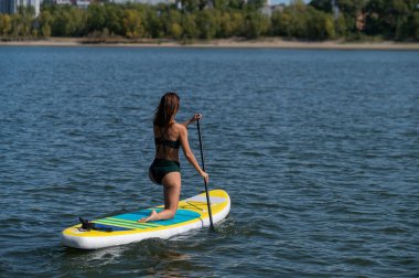 Gölde SUP sörf tahtası süren beyaz bir kadın. Yaz sporu