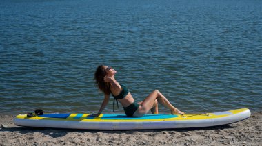 SUP panosunda poz veren beyaz bir kadın. Yaz sporu