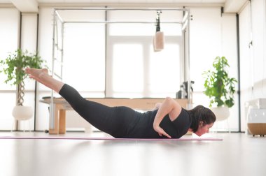 Tombul bir kadın stüdyoda pilates yapıyor.