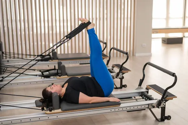 Aşırı kilolu beyaz kadın bir reformcu üzerinde pilates egzersizi yapıyor.