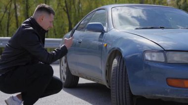 Kafkasyalı bir adam arabasındaki deformasyon fotoğraflarına bakıyor.