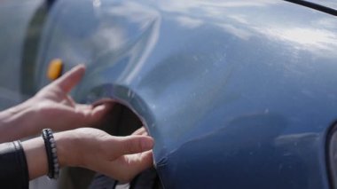 Beyaz adam inceler ve arabasındaki deformasyonu düzeltmeye çalışır.