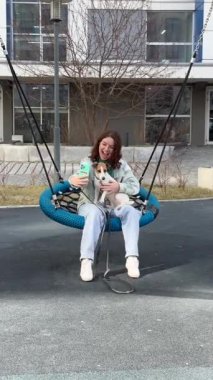 Beyaz kadın Jack Russell Terrier 'ını gezdirirken akıllı telefon kullanıyor.