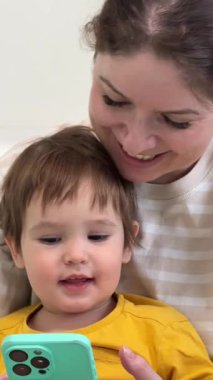 Beyaz kadın, küçük oğluyla birlikte akıllı telefona bakıyor.