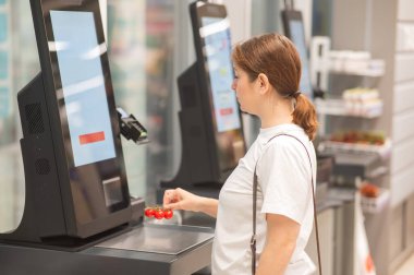 Bir kadın self-servis kasasında vişneli domates tartıyor.