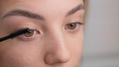 Genç bir kadının dikkatlice maskarasını kirpiklerine sürerken.