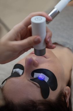 Bir usta, LED lamba kullanarak bir kadına kirpiklerini uzatır. Dikey fotoğraf