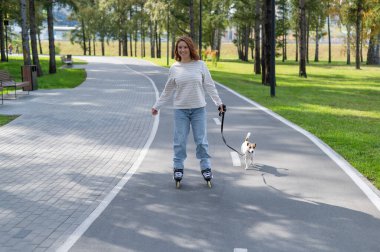 Beyaz kadın, Jack Russell Terrier köpeğiyle parkta paten kayıyor.