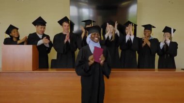 Tesettürlü mutlu Afrikalı kadın diploma alıyor ve sınıf arkadaşları onu alkışlıyor.