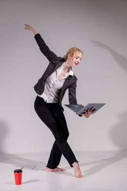 Beyaz arka planda iş elbisesiyle dans eden çıplak ayaklı balerin.