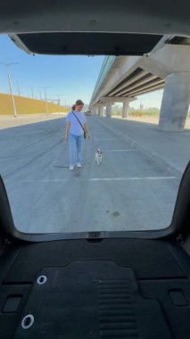 Beyaz kadın Jack Russell Terrier köpeğiyle bagaj kapısını kapatıyor.