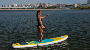 Gölde SUP sörf tahtası süren beyaz bir kadın. Yaz sporu