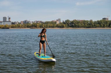 Gölde SUP sörf tahtası süren beyaz bir kadın. Yaz sporu