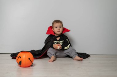 Beyaz arka planda kafatası tutan Drakula kostümlü küçük beyaz çocuk.