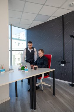 Beyaz adam çalışma masasında durmuş iş hakkında konuşuyor.