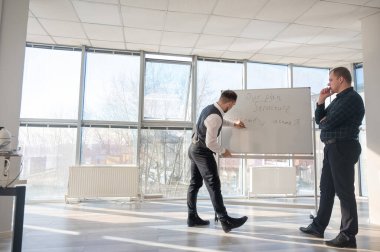 Beyaz bir kurulda iş tartışan iki beyaz adam.