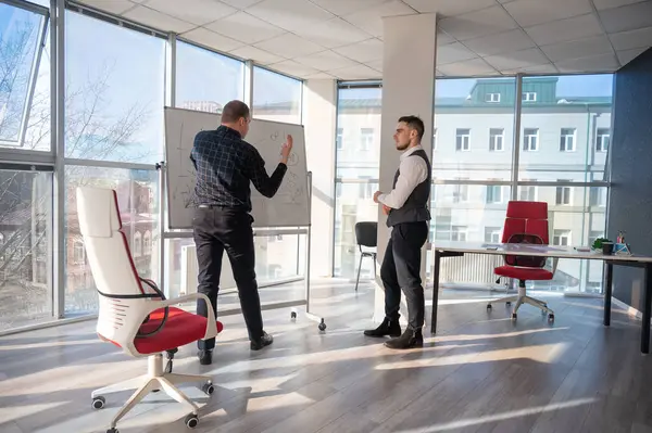 Beyaz bir kurulda iş tartışan iki beyaz adam.