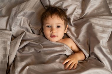 Beyaz tenli şirin bir çocuğun yatakta yatışının üst görüntüsü.