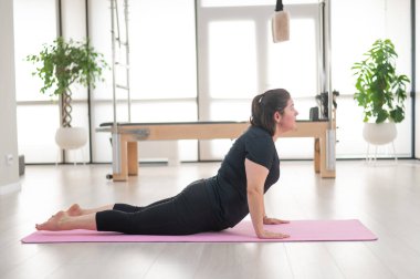 Tombul bir kadın stüdyoda pilates yapıyor.