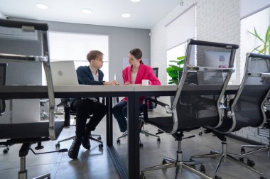 Kadın ve erkek ofiste otururken konuşuyorlar.