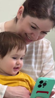 Beyaz kadın, küçük oğluyla birlikte akıllı telefona bakıyor.