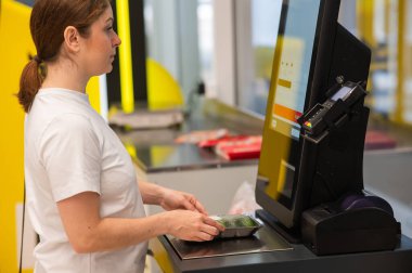 Bir kadın self-servis kasasında salatalık tartır.