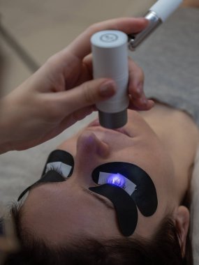 Bir usta, LED lamba kullanarak bir kadına kirpiklerini uzatır. Dikey fotoğraf