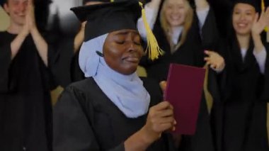 Tesettürlü mutlu Afrikalı kadın diploma alıyor ve sınıf arkadaşları onu alkışlıyor.