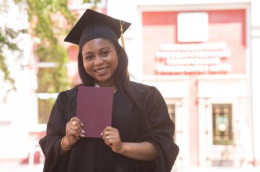 Mezuniyet elbisesi içinde diploması olan mutlu, genç bir Afrikalı kadın.