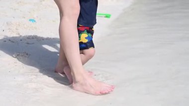 Kadın bacaklarının ve deniz kıyısındaki bir yaşındaki çocuğunun yakın çekimi.