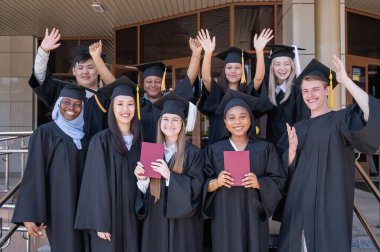 Farklı uluslardan mutlu öğrenciler mezuniyet elbiseleriyle diplomalarını tutuyorlar.