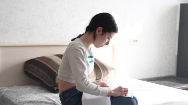 Genç beyaz kadın yatakta otururken çapraz dikiş atıyor.