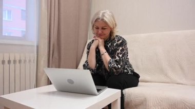 Kanepede otururken laptop kullanan olgun bir kadın.