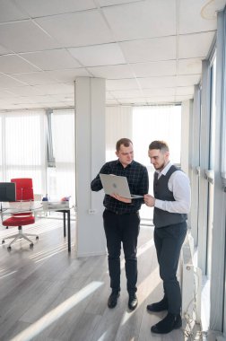 İki beyaz adam dizüstü bilgisayara bakıyor ve iş tartışıyorlar.