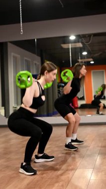 İki beyaz kadın halterle çömeliyor.