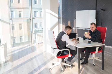 Masada otururken akıllı telefon kullanan iki beyaz adam.