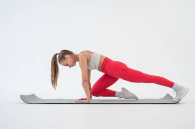 Genç bir kadın beyaz arka planda kalas egzersizi yapıyor.