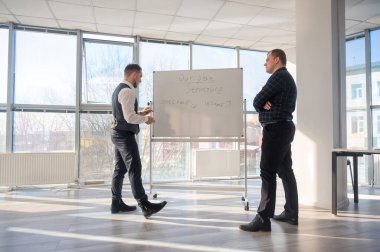 Beyaz bir kurulda iş tartışan iki beyaz adam.