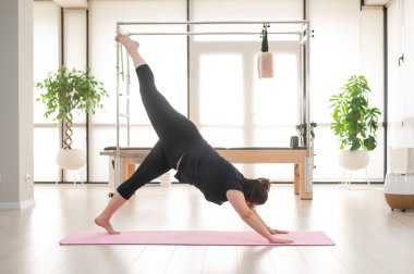 Tombul bir kadın stüdyoda pilates yapıyor.