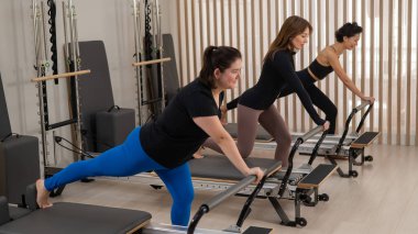 Üç Asyalı kadın bir reformcu üzerinde pilates yapıyor.