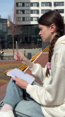 Açık havada kalemle çizim yapan beyaz bir kadın.