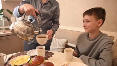 Orta yaşlı beyaz bir kadın iki oğluyla yemek yiyor. Aile çay partisi.